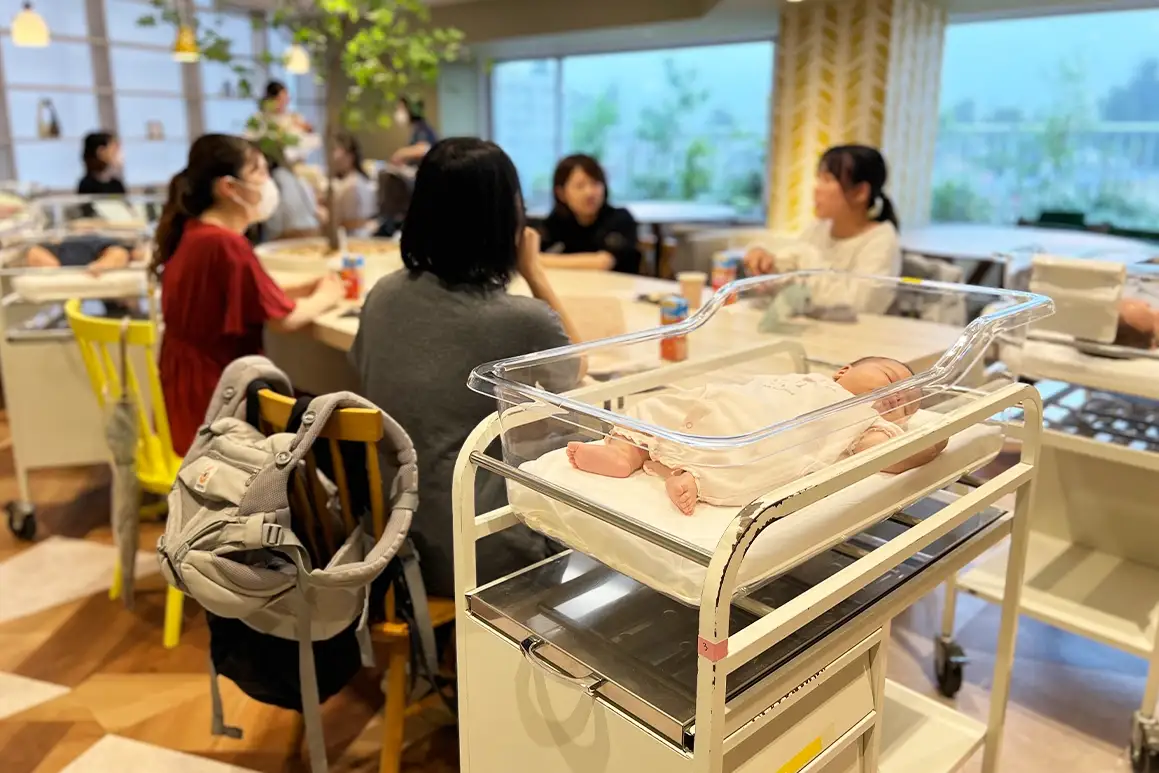 同窓会で談笑するお母さんたちと、ベビーベッドで眠る赤ちゃん